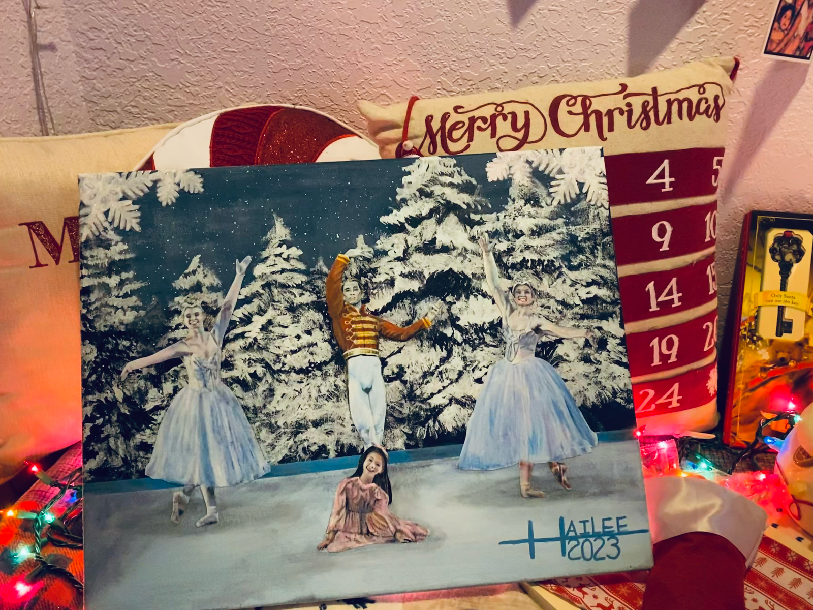  a rectangular painting inspired by the nutcracker play. four ballerinas stand on stage. in the center of the stage the nutcracker prince stands while clara sits on the floor by his feet. two ballerinas wearing white skirts stand on opposite sides of the prince.